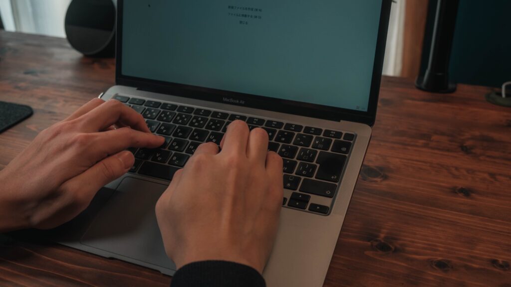 木製デスクに置いたMacBook Airのキーボードを、両手で打っているところ